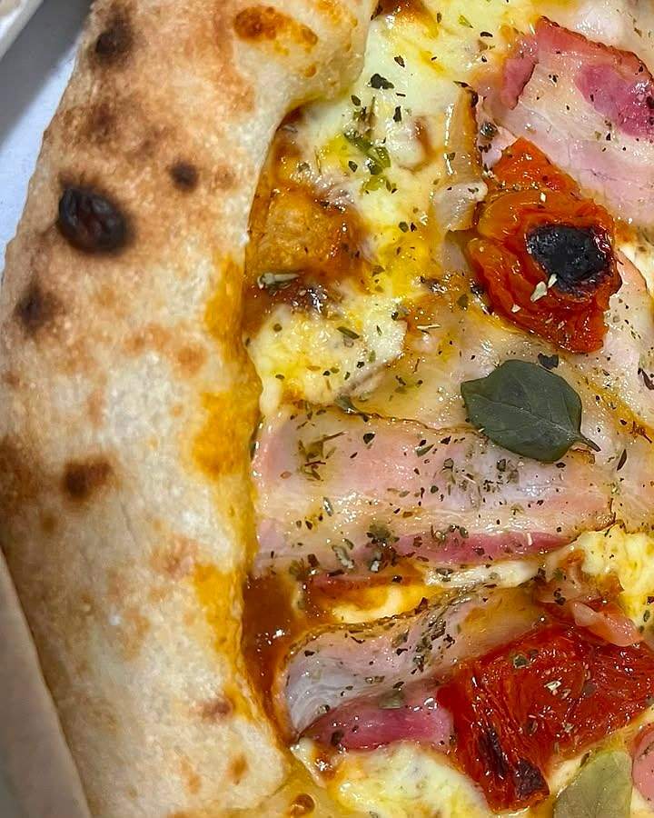 Detalhe da pizza Bella Itália, com tomate seco, bacon, manjericão e a borda tostada